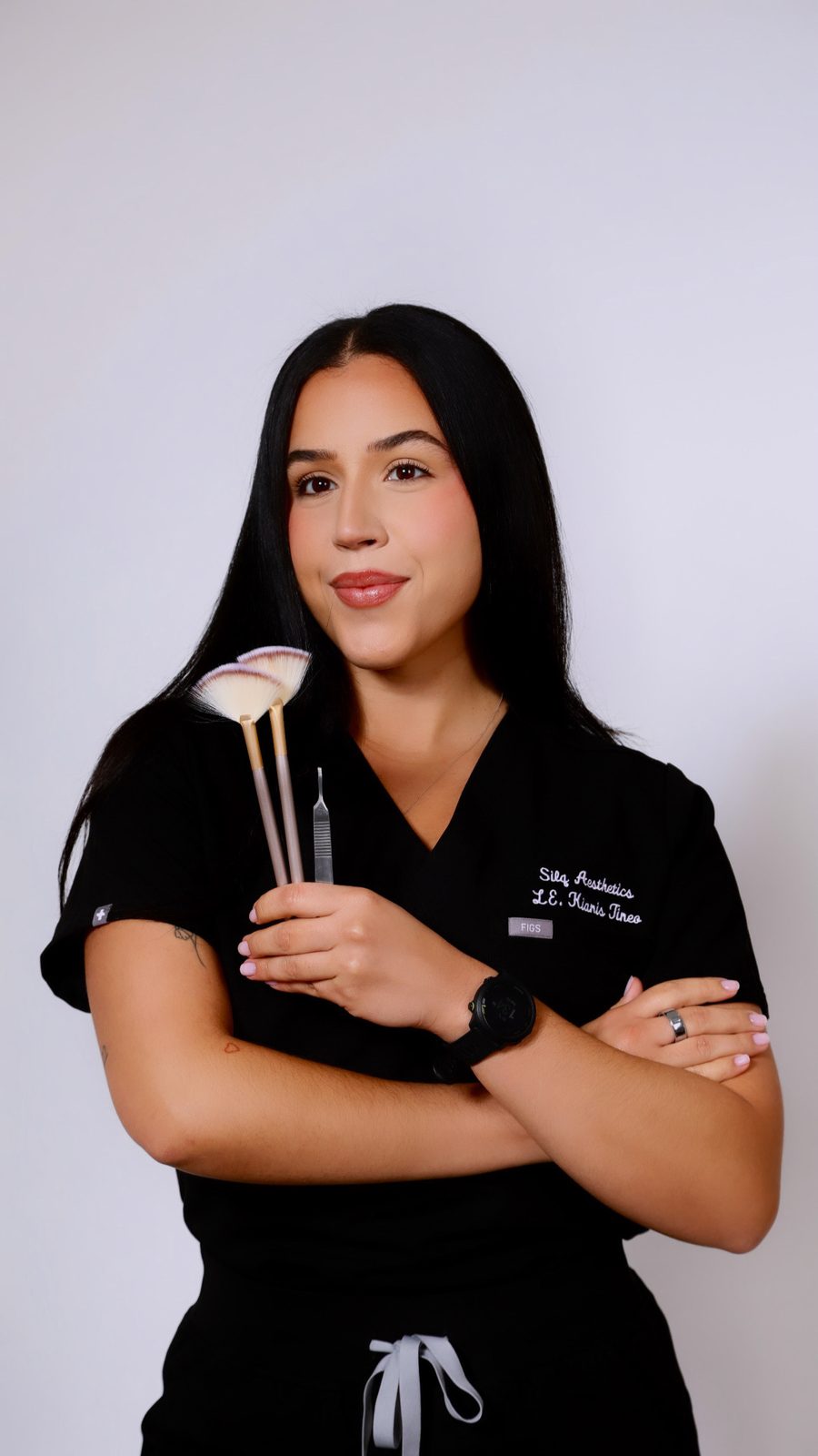 Kianis Tineo, licensed esthetician and founder of Silq Skin Aesthetics, in her Silq scrubs holding a fan brush