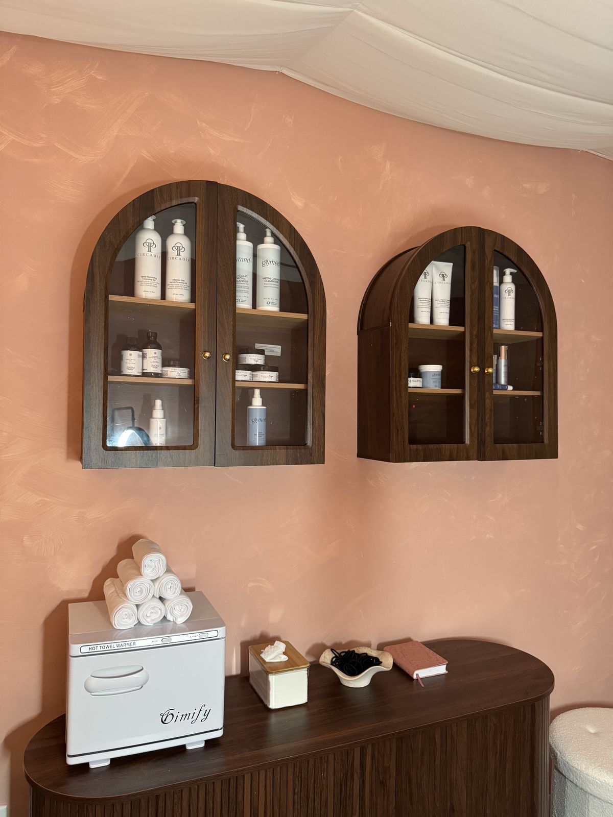 Arched shelves of professional skincare products on a blush wall